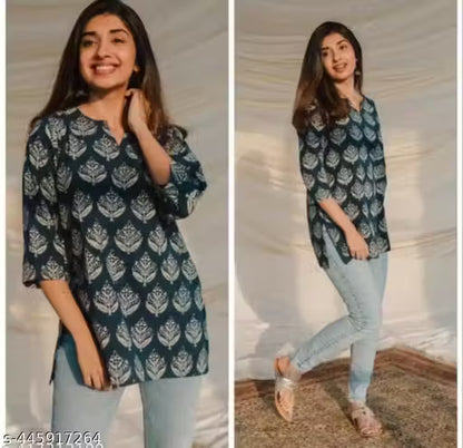 Woman wearing a dark blue patterned top and light blue jeans indoors.